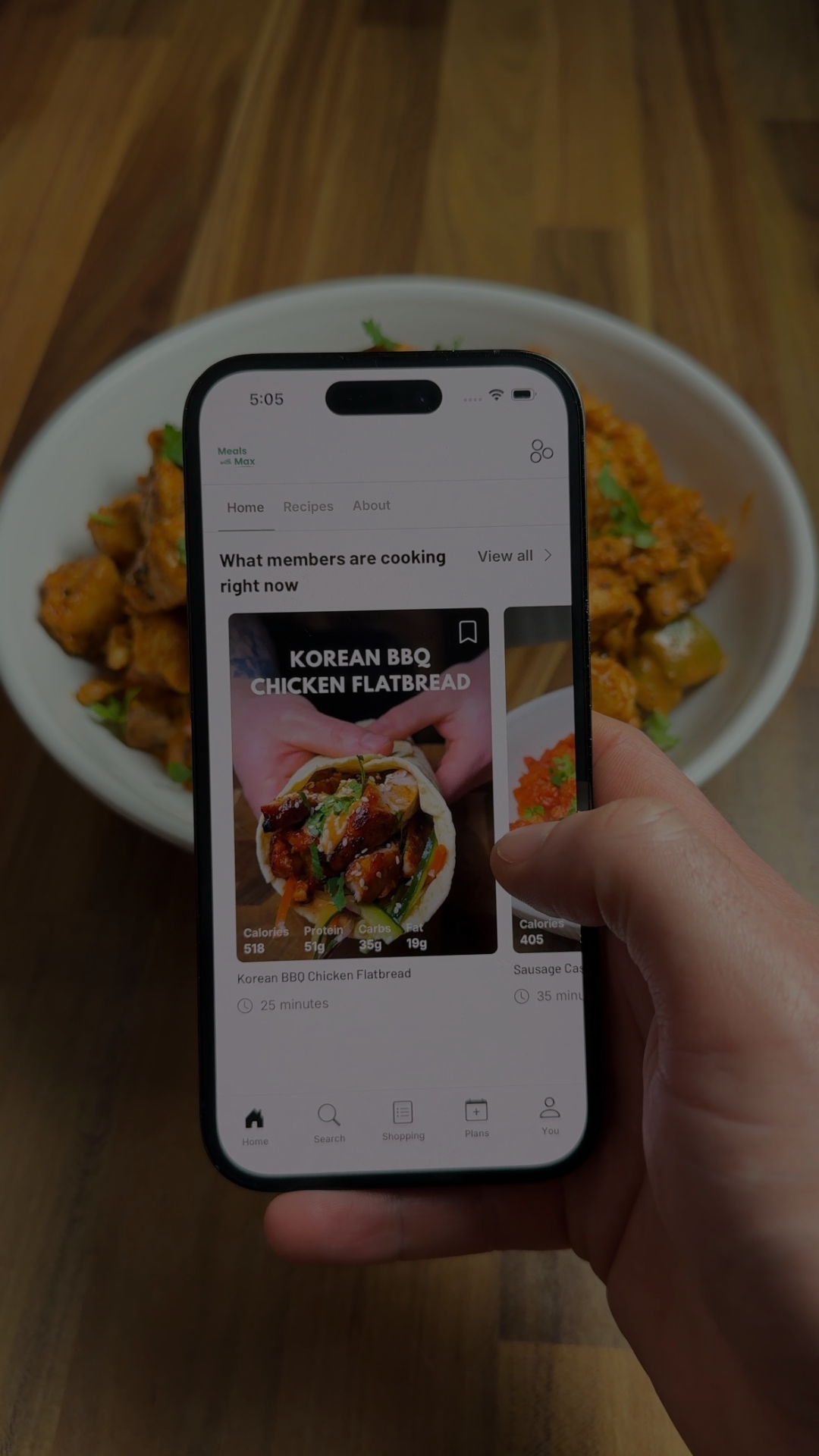 Hand holding a phone with the Meals with Max app open, showing a recipe over a bowl of food